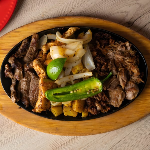 Sizzling fajita platter with steak, chicken, carnitas, onions, potatoes, lime, and jalapeño.