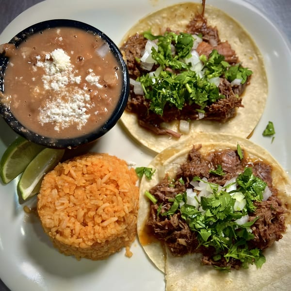 Two Habaneros Mexican Grill tacos with shredded meat, cilantro, onions, rice, and refried beans.