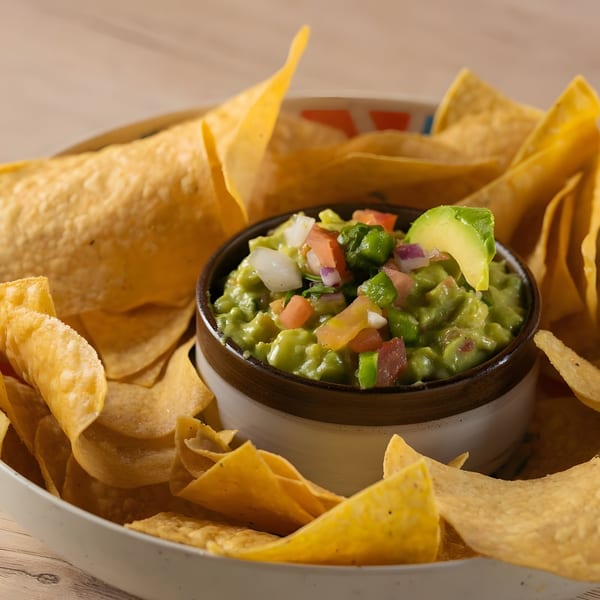 Fresh guacamole topped with diced tomatoes, onions, and avocado slices, surrounded by tortilla chips.