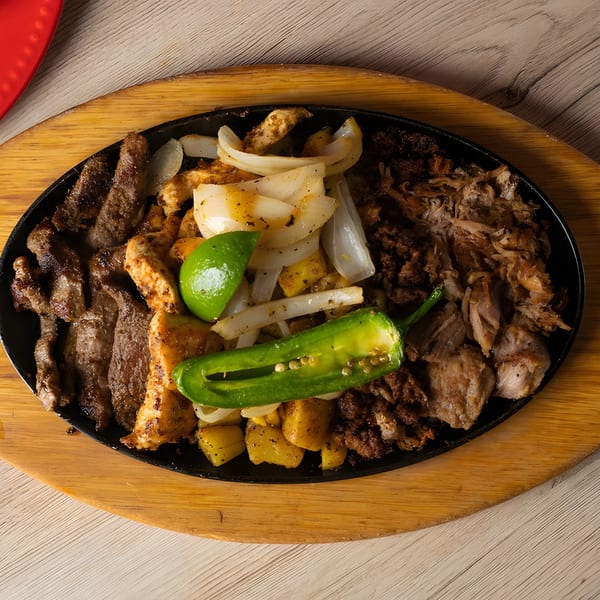 Sizzling Mexican fajita platter with steak, chicken, carnitas, onions, potatoes, lime, and jalapeño.