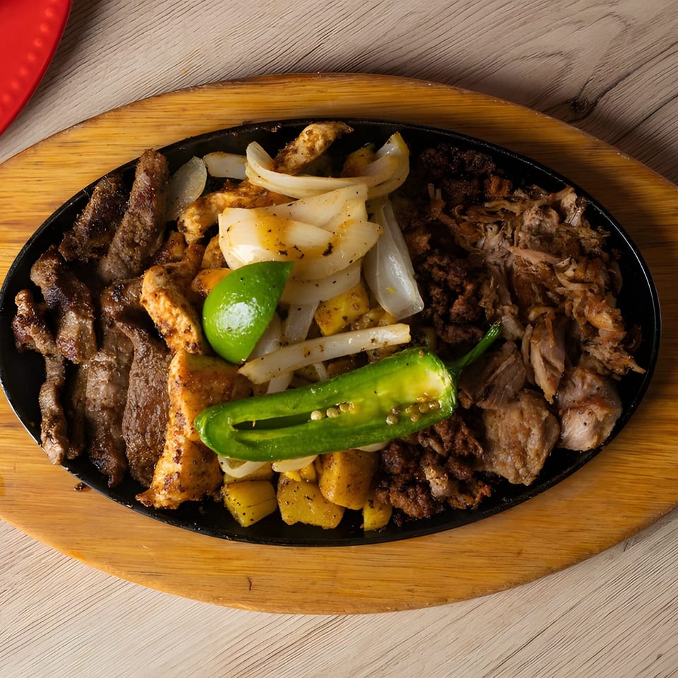Sizzling Mexican fajita platter with steak, chicken, carnitas, onions, potatoes, lime, and jalapeño.