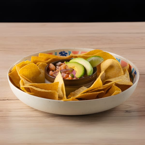 A white bowl filled with tortilla chips surrounds a smaller bowl of ceviche, avocado, and lime.